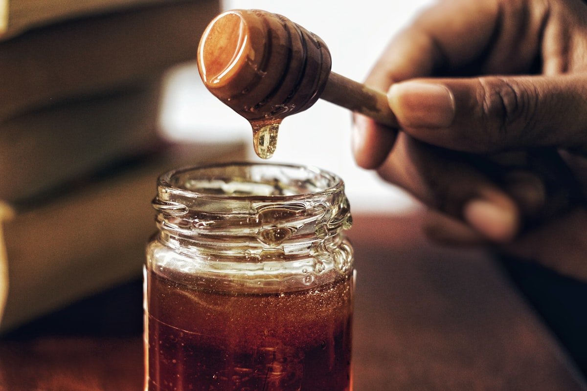 Natural honey dripping from a dipper into a jar
